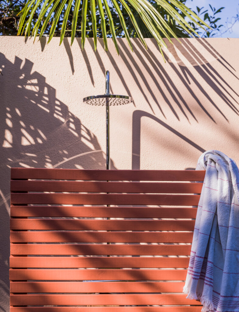 屋外のシャワースペースの画像。壁は、No.231 Setting Plasterの淡いピンク、ウッドスクリーンは、No.64 Red Earthのテラコッタのような赤褐色の色で仕上げています。2色の朗らかで温かさに満ちた色合いは、陽光に照らされることでより魅力を増しています。