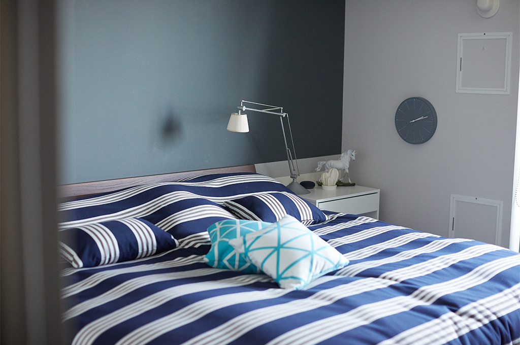 ヘッドボード側の壁面に、深みのあるFarrow & Ballのダークカラーを配したアクセントウォール。ストライプのリネンやミニマルな照明とのコントラストが美しく、マットで上質なペイントの質感が、寝室に落ち着きとモダンな品格を与えています。