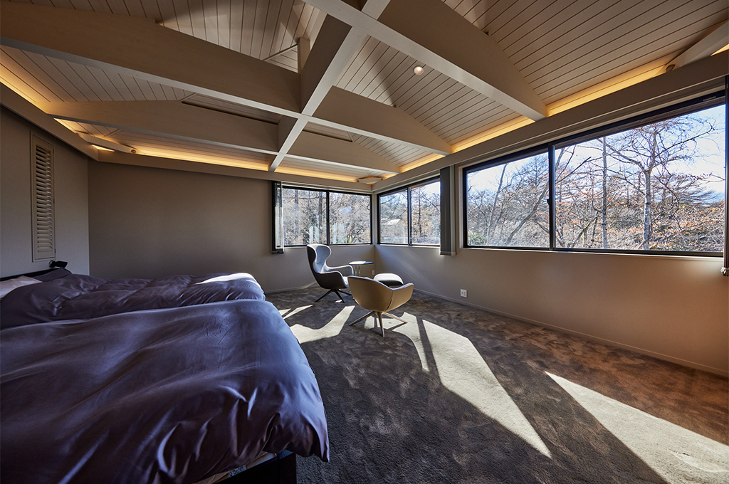 大きな窓から注ぐ光が、Farrow & Ballで彩られた勾配天井と梁を優しく照らす開放的な寝室。温かみのあるニュアンスカラーが、室外の木々と室内をシームレスに繋ぎ、自然のぬくもりを感じながらゆったりと過ごせる極上のリラックス空間を実現しています。