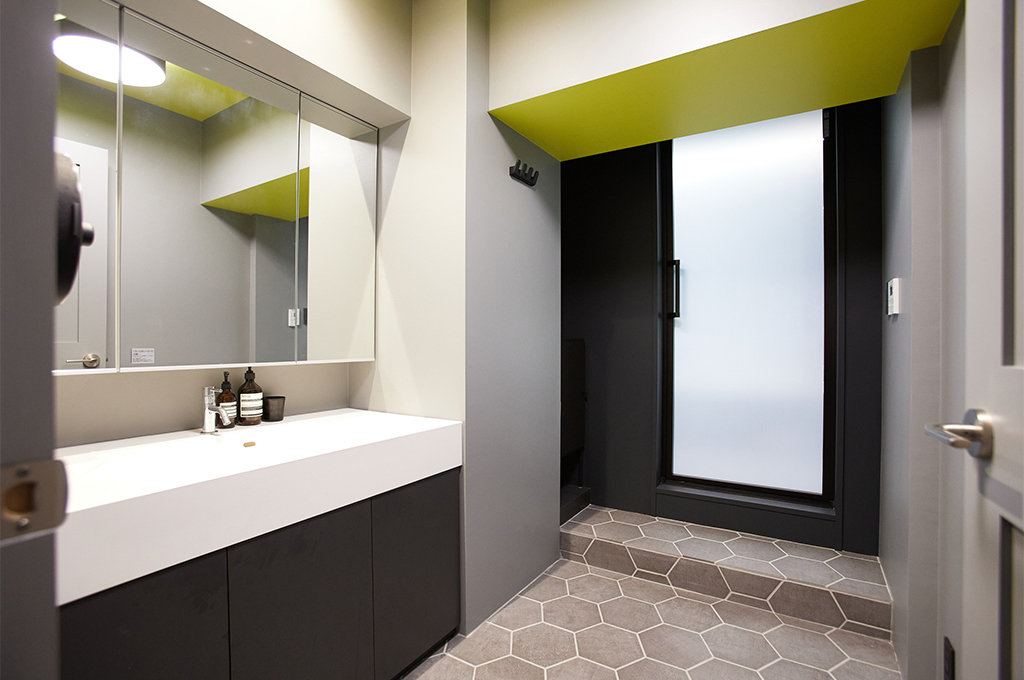 グレーのベースカラーに、鮮やかなイエローのペイントを天井に配した遊び心溢れる洗面室。Farrow & Ballのマットな質感が、ヘキサゴンタイルの床やモダンな設備と相まって、エッジの効いたスタイリッシュで都会的なサニタリー空間を形作っています。