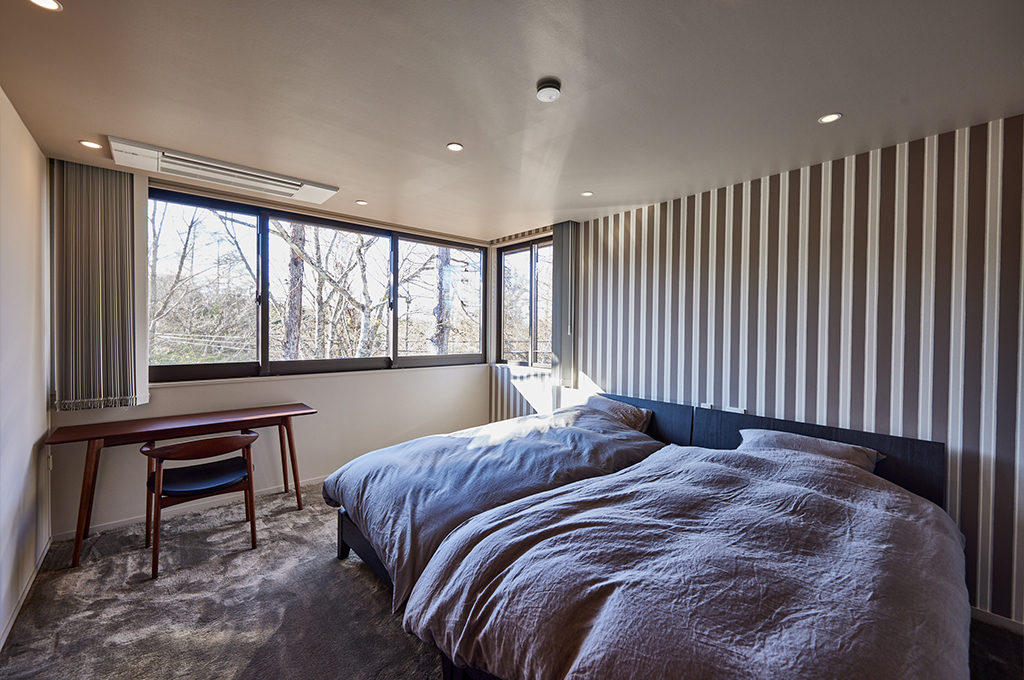 シックなストライプの壁紙と柔らかなニュアンスカラーのペイントを組み合わせた寝室。Farrow & Ballならではの奥行きのある質感が、窓からの自然光を優しく受け止めます。モダンな家具と調和し、心から安らげる上質な大人びた休息空間を創り上げています。