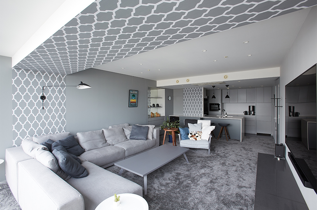 Farrow & Ballのグレーペイントと、幾何学模様の壁紙が美しく調和したモダンなリビング。壁から天井へと続くアクセントクロスが奥行きを与え、キッチンまで統一されたグレーのグラデーションが、洗練された上質なインテリア空間を演出しています。