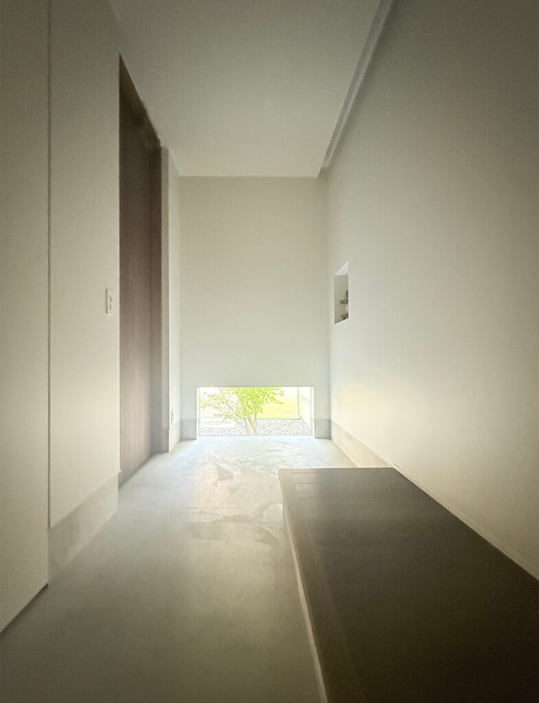 玄関ホールのニッチに飾られた盆栽と、光を柔らかく反射するペイント壁。No.2001 Strong White（ストロングホワイト）