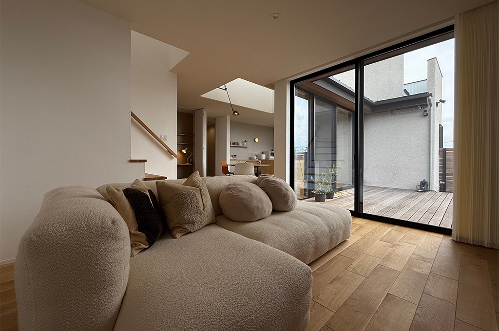 Farrow & Ballの柔らかなニュートラルカラーが包み込むリビング。無垢材のフローリングとテラスが繋がる開放的な空間で、高品質な塗料が生み出す奥行きのある壁色が、上質な家具や自然光と調和し、心安らぐ住まいを演出しています。