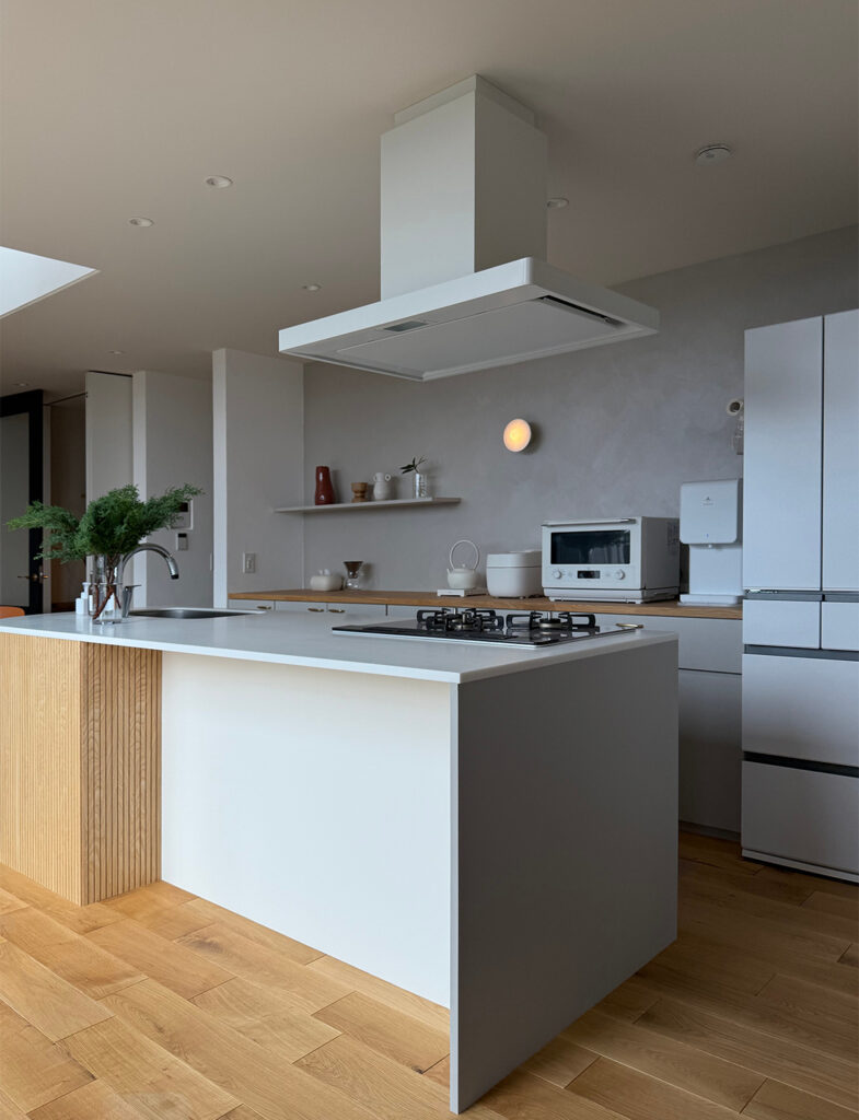 キッチン背面を彩る、「Moire（モアレ）」仕上げ。職人の手作り感のある意匠性と、繊細な光沢のあるメタリックな質感が、水回りにも安心の機能性とデザイン性を両立し、ディスプレイを引き立てる上質な壁面を実現しています。