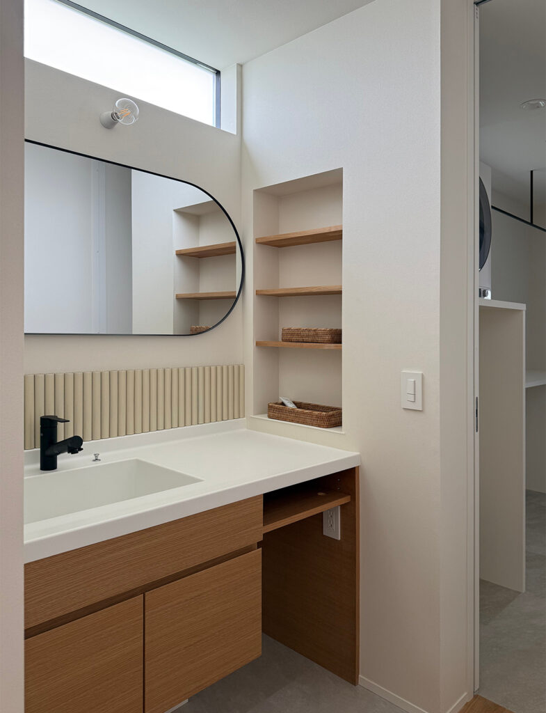 柔らかなホワイトが、木目調の洗面台と調和する清潔感あふれるサニタリー。高窓からの自然光がペイントの質感を美しく際立たせ、ニッチ収納やタイル状の装飾がアクセントを添える、モダンで温もりのある洗面空間の施工例です。