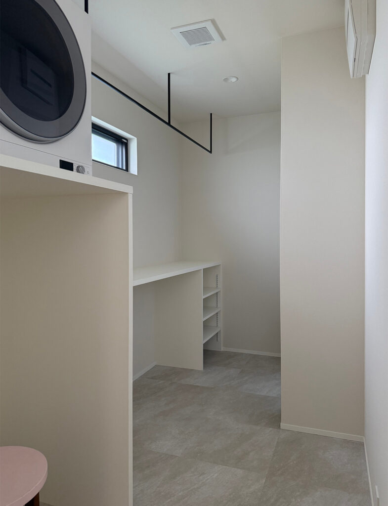 明るいニュートラルカラーが、家事の時間を心地よく彩るランドリールーム。黒のアイアンバーが空間を引き締め、マットな壁面とグレーのフロアタイルが洗練された清潔感を演出します。実用性とデザイン性を両立した、モダンな施工例です。