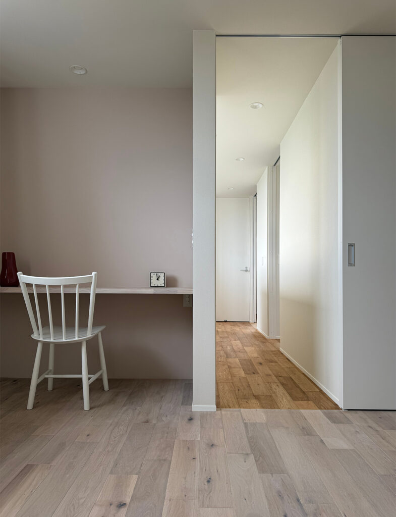 ニュアンスカラーが美しいワークスペース。くすみカラーの壁が白いチェアや木目調のフローリングと調和し、モダンで落ち着いたインテリアを演出しています。自然光が優しく回る、洗練された北欧スタイルの書斎レイアウトです。