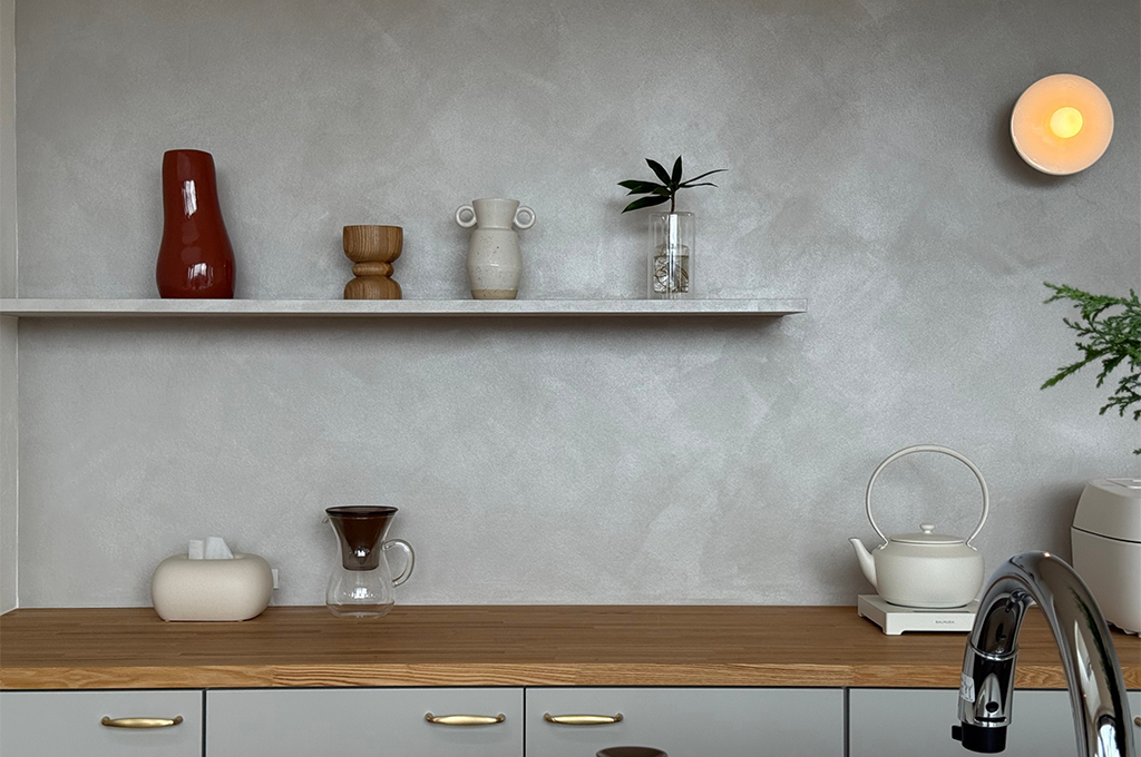 キッチン背面を彩る、「Moire（モアレ）」仕上げ。職人の手作り感のある意匠性と、繊細な光沢のあるメタリックな質感が、水回りにも安心の機能性とデザイン性を両立し、ディスプレイを引き立てる上質な壁面を実現しています。