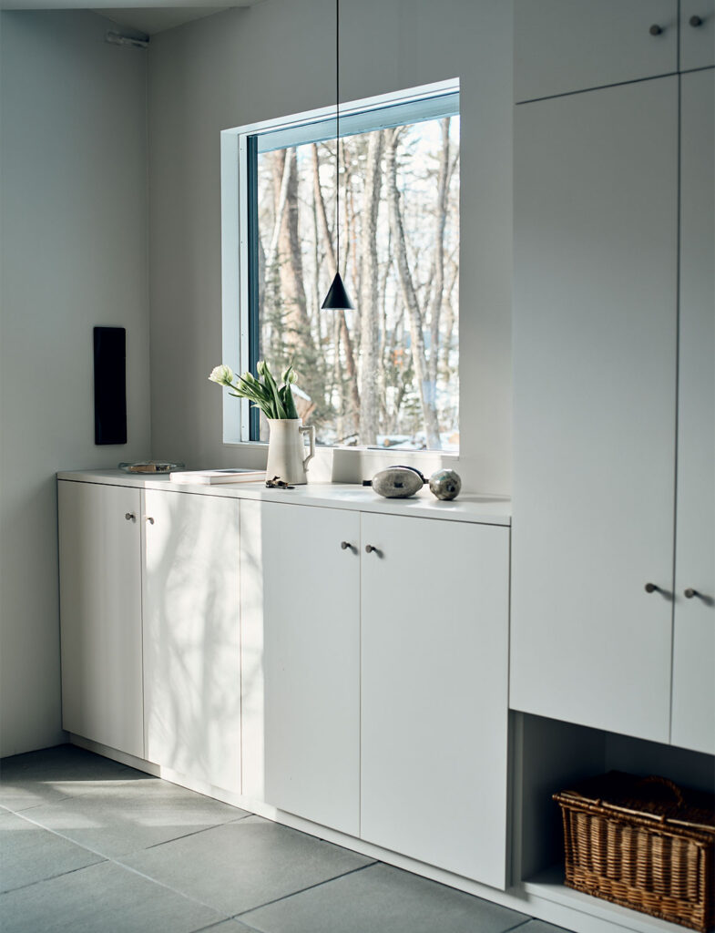 インテリアスタイリスト・黒田美津子さんのアトリエにある、光と影が交差する廊下のしつらえ。白いマットな収納扉には、窓外の木々が映し出す繊細な影が描かれ、自然の息吹が室内へと溶け込んでいる。窓辺のピッチャーに生けられた白いチューリップと、空間をモダンに引き締める細身のペンダントライトが、静謐な美しさをいっそう際立たせている。