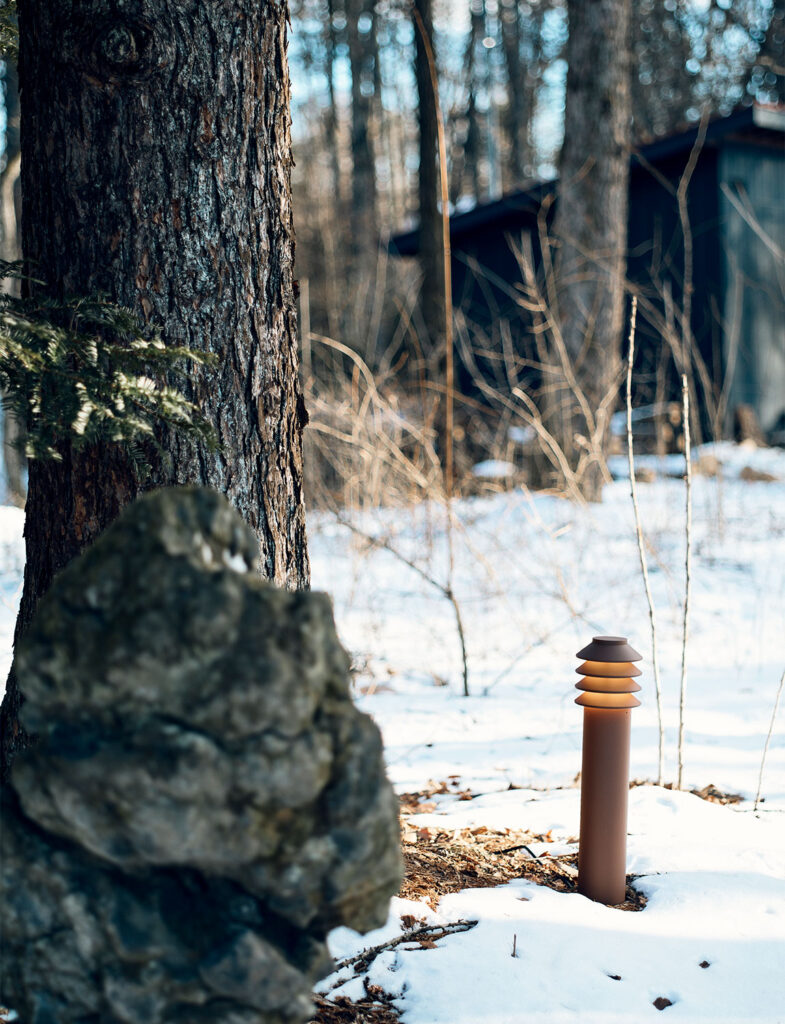 冬の林に静かに灯る、ルイスポールセン（Louis Poulsen）を彷彿とさせる北欧デザインのガーデンライト。雪に覆われた地面と深い森の青白いトーンの中で、ポールから漏れる温かな光が、黒田美津子さんのアトリエが持つ「安らぎ」を象徴している。自然の厳しさと、計算された照明計画による美しさが同居する、アトリエの環境を物語る一枚