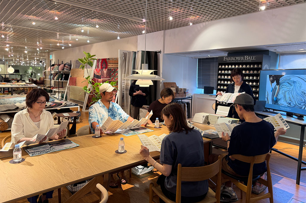 ザ・コンランショップ 新宿店でのFarrow & Ballワークショップにて、参加者が一斉にカラーチャート（カラーカード）を広げて寝室の色選びを楽しむ様子。奥ではスタイリストが大きなカラーサンプルを提示し、右側のモニターにはペイントの製造風景が映っている。