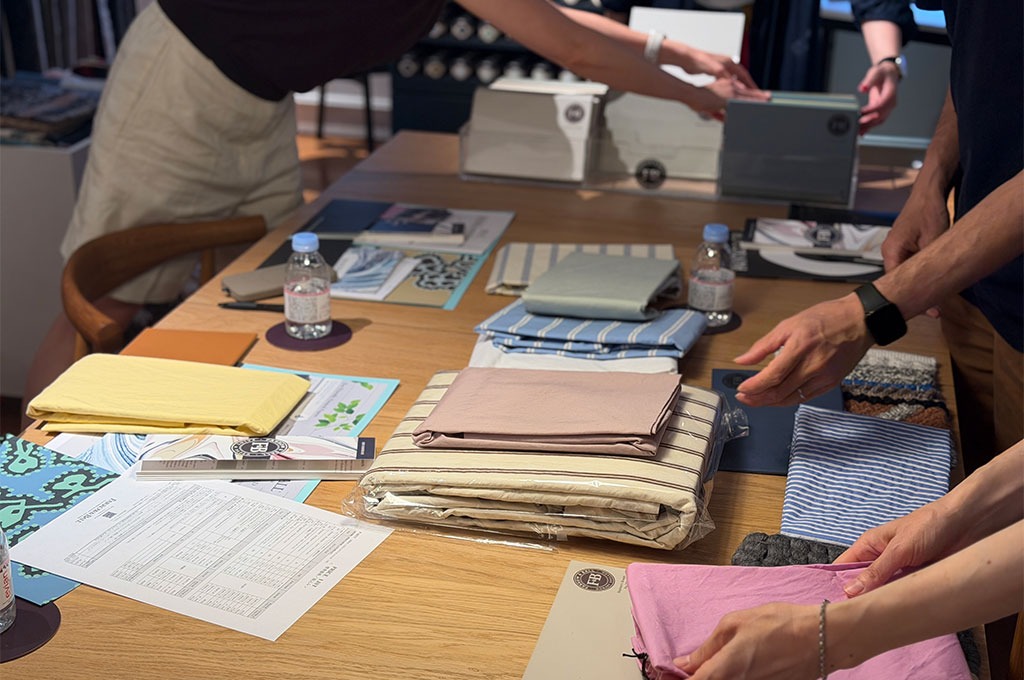 ザ・コンランショップ 新宿店でのワークショップにて、Farrow & Ballの様々なペイントサンプルボードと、TEKLAやkvadratなどの上質なファブリックリネン、ラグサンプルを大きなテーブルの上に広げて、理想の寝室コーディネートを熱心に組んでいる参加者たちの手元風景。