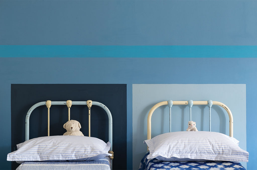 壁（ベースカラー）：No.237 Cook's Blue / 壁（ライン）：No.280 St Giles Blue  / ベッドヘッド（左）：No.281 Stiffkey Blue / ベッドヘッド（右）：No.89 Lulworth Blue
ベッドが2台置かれているお部屋に、さまざまなブルーでペイントされた施工事例。一色だけでなく、多色で彩られているにも関わらずうるさく感じないのは、同じブルー系統の濃淡でコーディネートされているからでしょう。