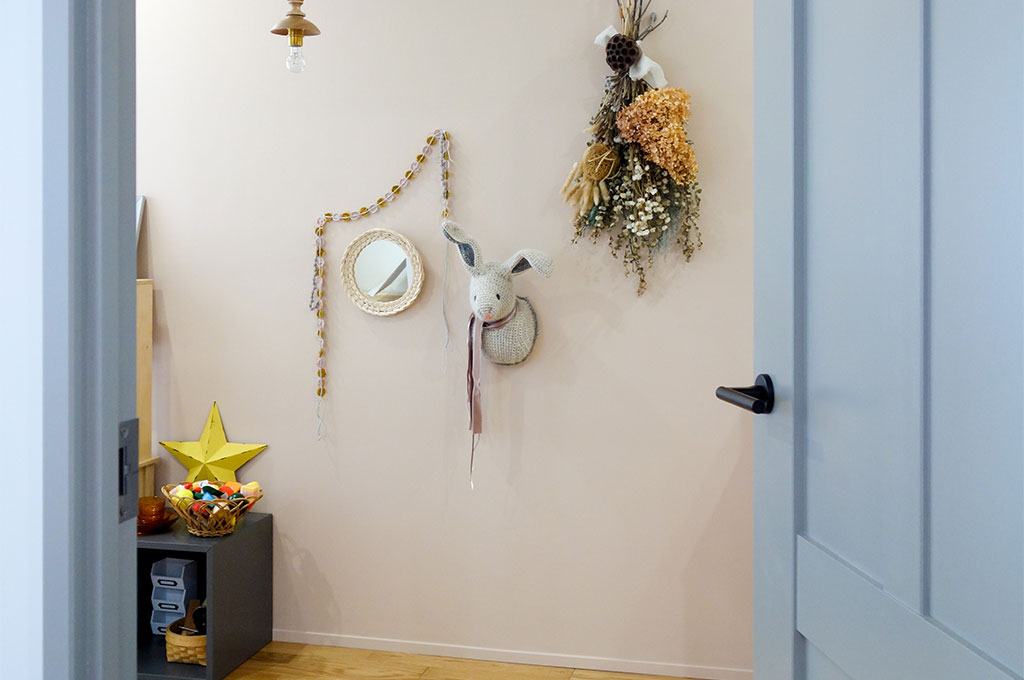 E様邸：壁：No.231 Setting Plaster
グレーのドアを開けた先の子供部屋の壁には、穏やかで優しげなピンクであるNo.231 Setting Plasterが塗装されている。そこに花やアートフルなぬいぐるみ、おもちゃなどが飾られている部屋。